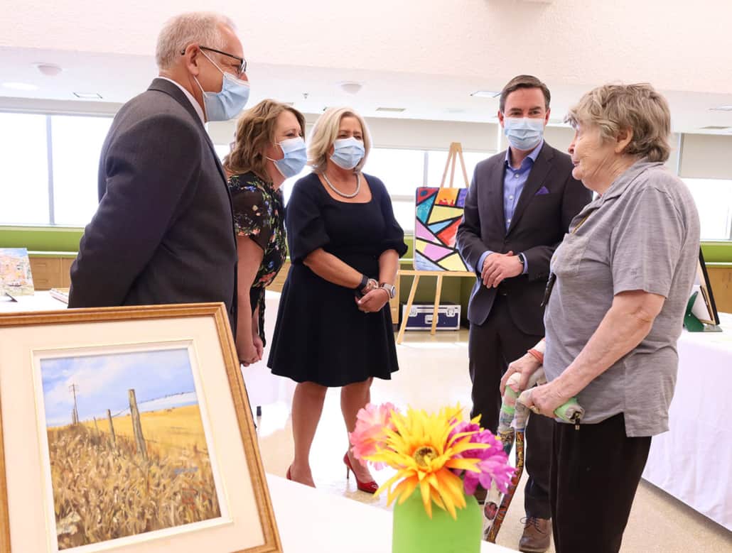 Dr. Al Kryski, Board Chair, Bethany Care Society, Jennifer Vance, Bethany Calgary Site Administrator, Jennifer McCue, President and CEO of Bethany Care Society, and Jason Copping, Alberta Health Minister, chat with Bethany Calgary long-term resident, Avril. Artwork in foreground.